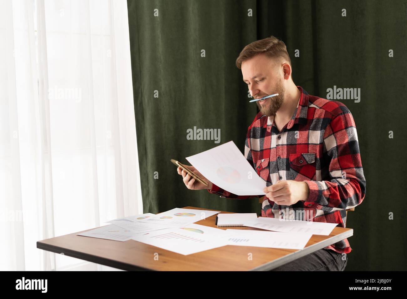 Uomo caucasico concentrato in casual wear guardando attraverso il rapporto di ricerca di marketing, l'analisi dei dati statistici in grafici, lo sviluppo di strategia di crescita Foto Stock