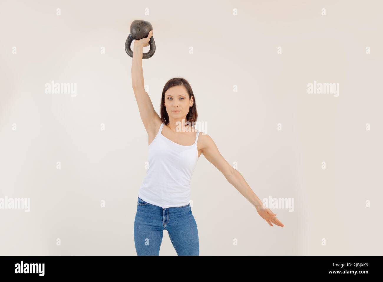 Giovane atletica donna che solleva Kettlebell e mette giù il braccio, sfondo bianco. Mantenersi in forma grazie all'allenamento di forza e al sollevamento pesi in palestra, pompando Foto Stock