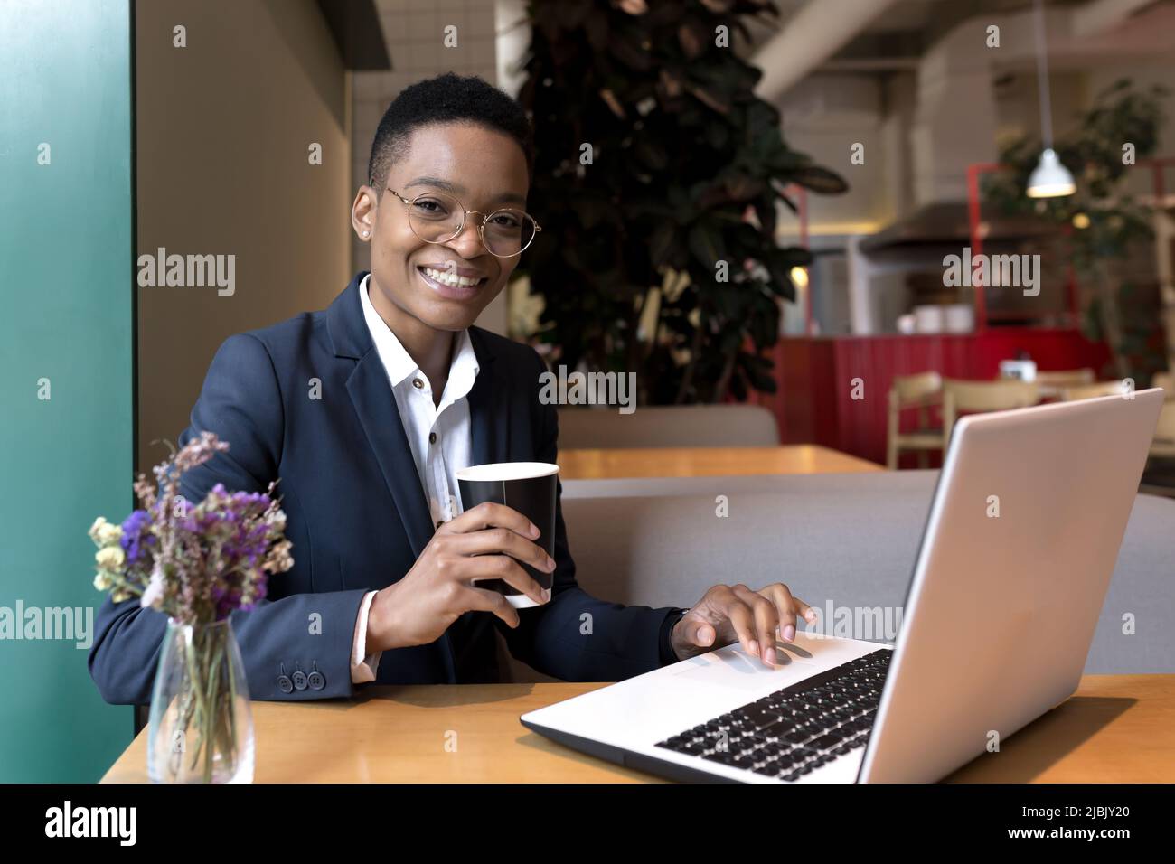 Giovane bella donna afroamericana che lavora in un caffè, a pranzo pausa, usando il laptop, donna d'affari sorridendo e rallegrandosi nel successo guardando camer Foto Stock