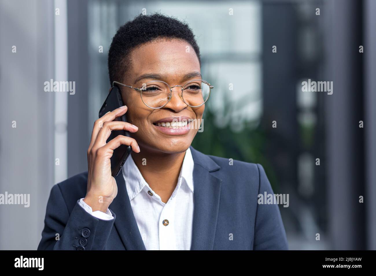 Foto di primo piano ritratto di giovane bella donna da lavoro, afroamericana che parla al telefono, sorridente e rallegrante guardando felice camer Foto Stock