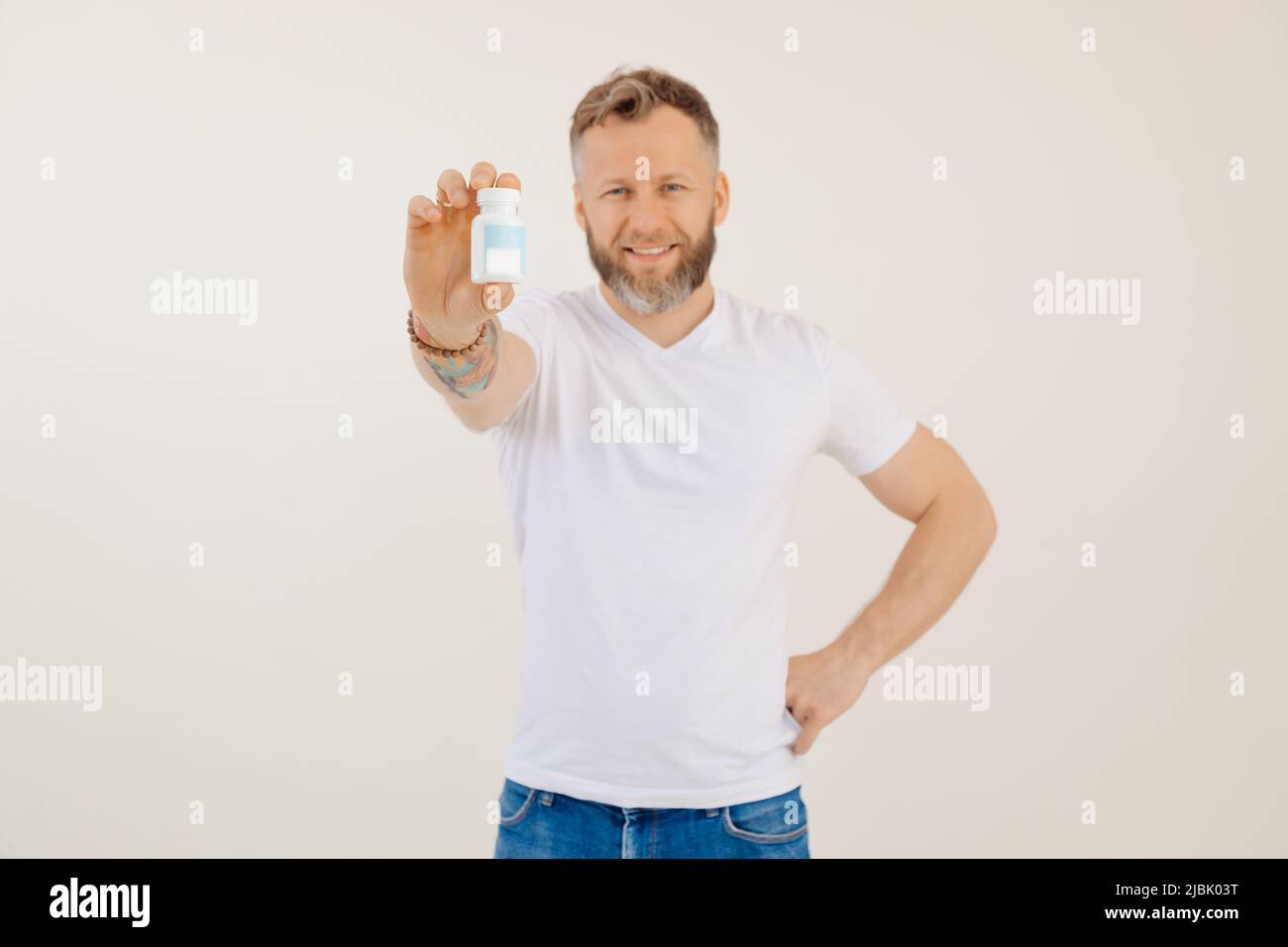 Ritratto di giovane uomo sorridente che fa pubblicità a vitamine utili per gli uomini, sfondo bianco. Tenendo in mano e puntando al vaso di pillole, trattamento della malattia Foto Stock