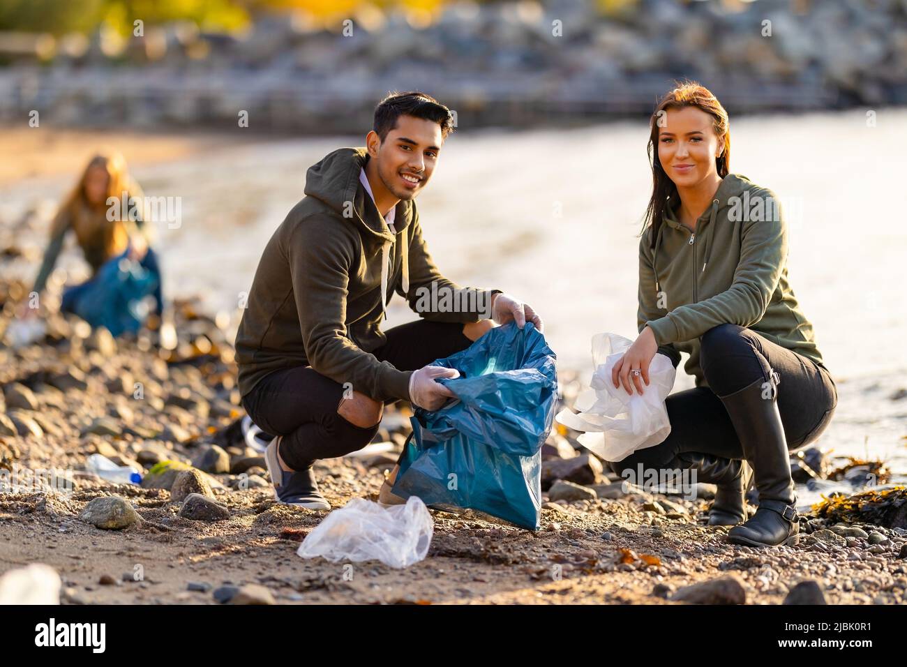 Team di volontari dedicati e sorridenti che raccolgono rifiuti di plastica in spiaggia Foto Stock