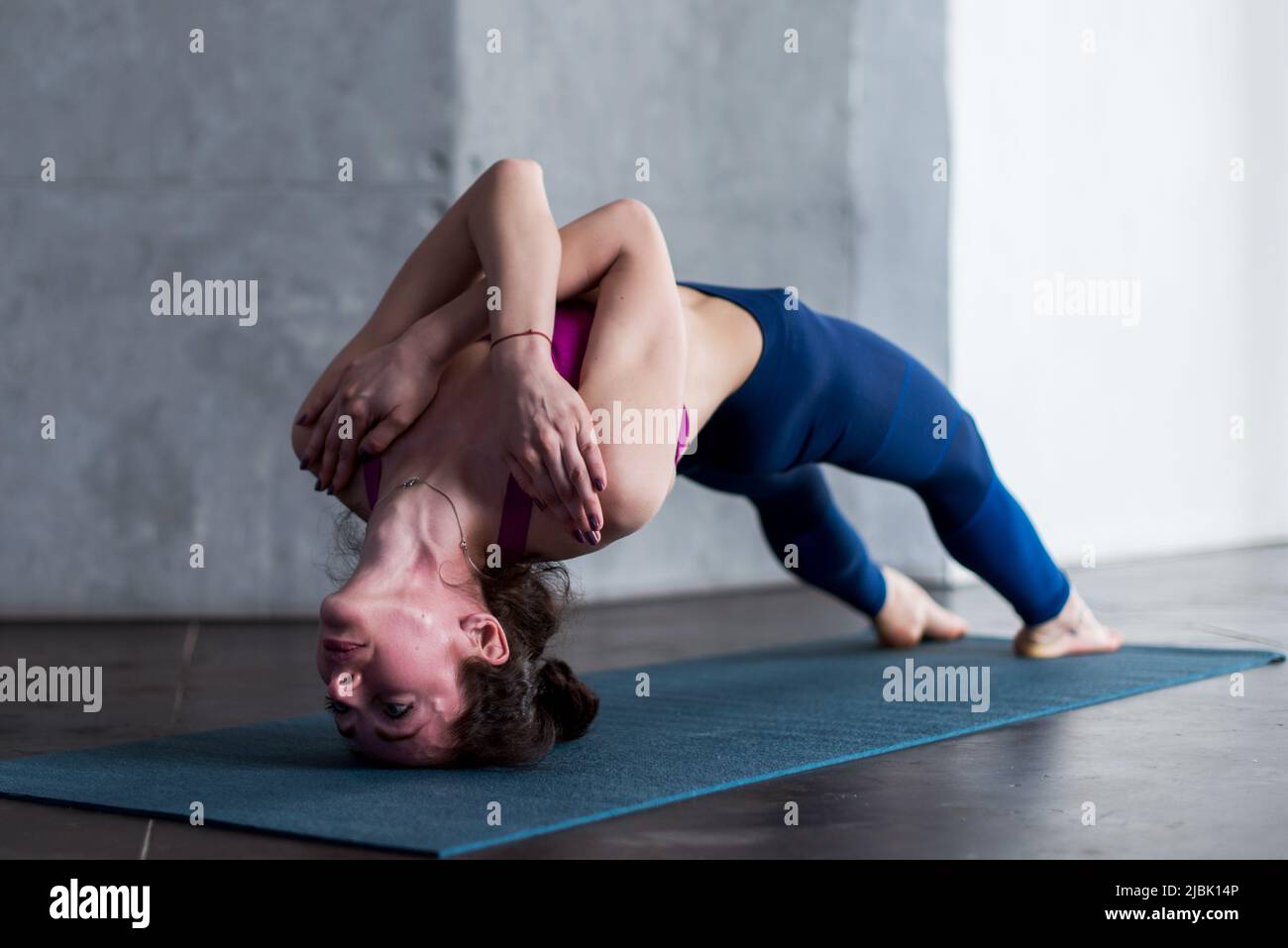 Giovane donna caucasica che fa impegnativo capezzale backbend yoga posa con le braccia incrociate sul petto. Foto Stock