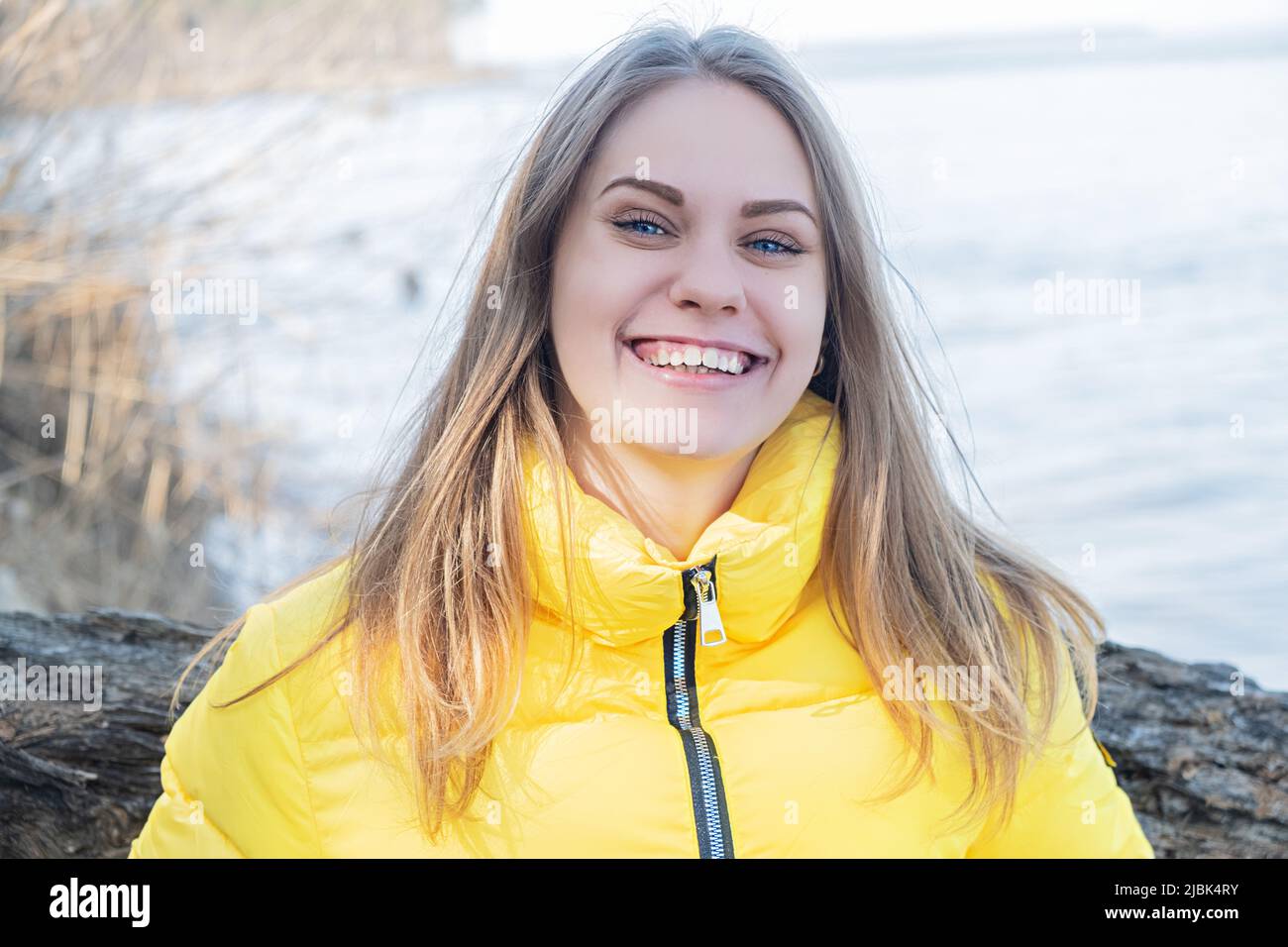 Ritratto di sorridente ragazza felice guardando in macchina fotografica sullo sfondo di un lago nella foresta. Salute mentale. Donna che indossa giallo brillante Foto Stock