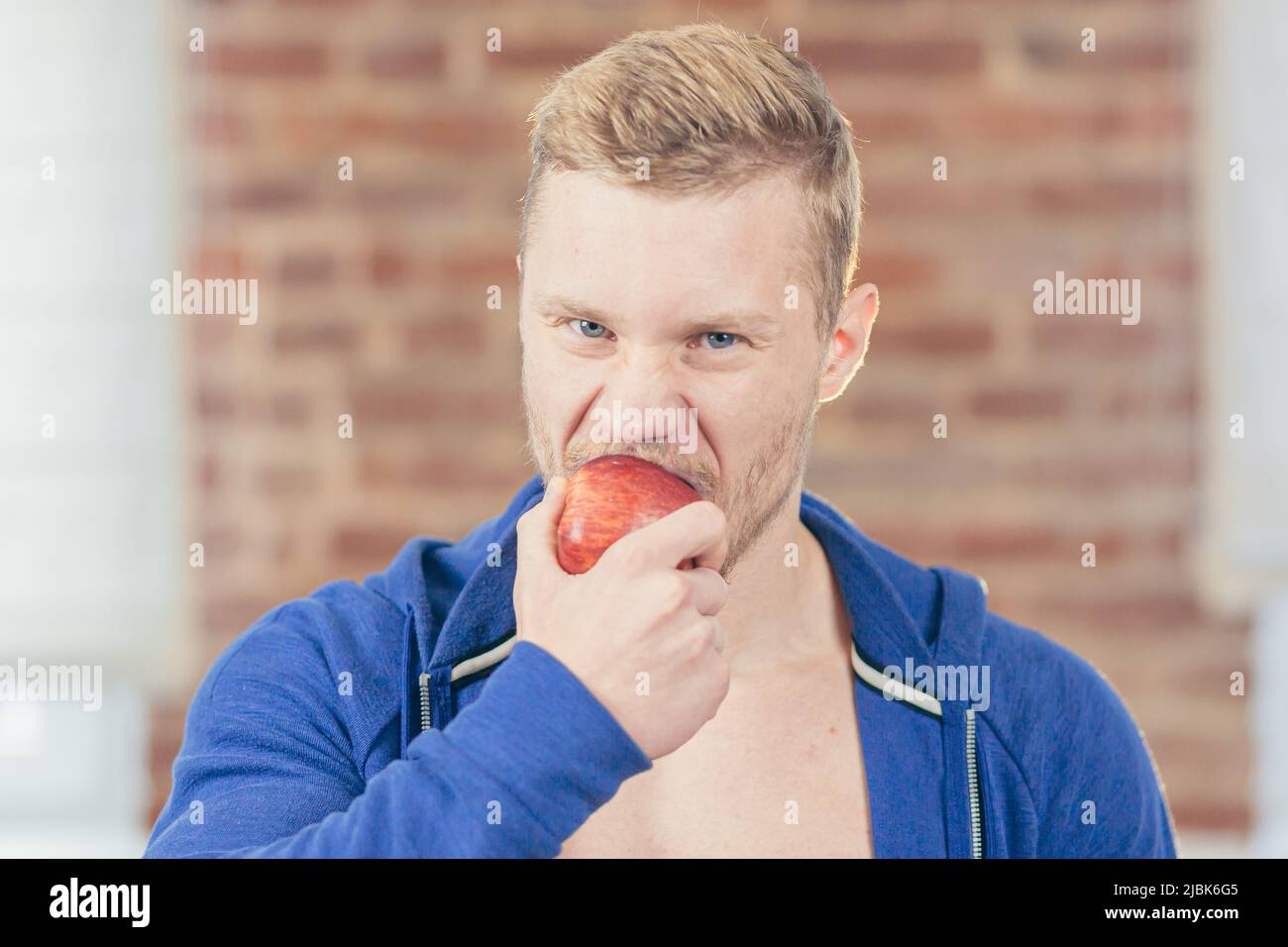 Foto da vicino. Ritratto di giovane atletico bello uomo che mangia mela in cucina a casa, facendo succhi freschi e Macedonia di frutta, guardando camer Foto Stock