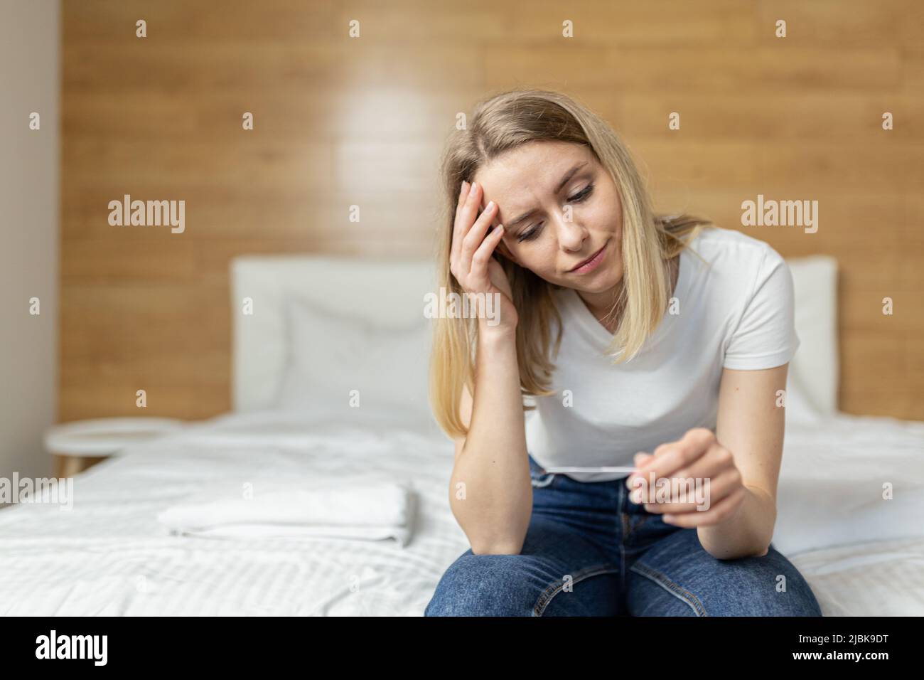 Giovane bella donna a casa seduta sul divano, tenendo un test di gravidanza veloce nelle sue mani, sconvolto, scioccato, imparato la gravidanza, pensa confu Foto Stock