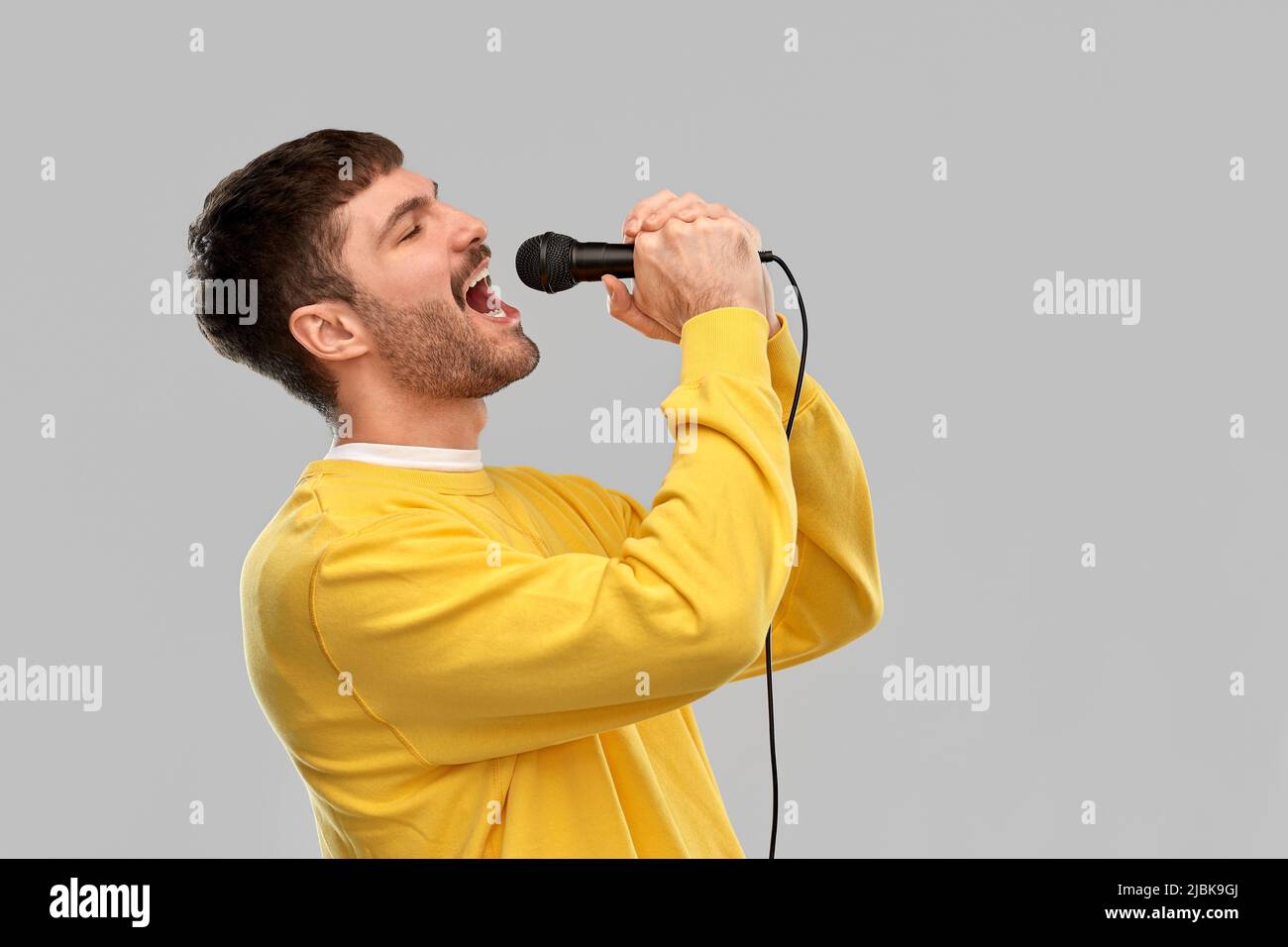 uomo in felpa gialla con microfono che canta Foto Stock