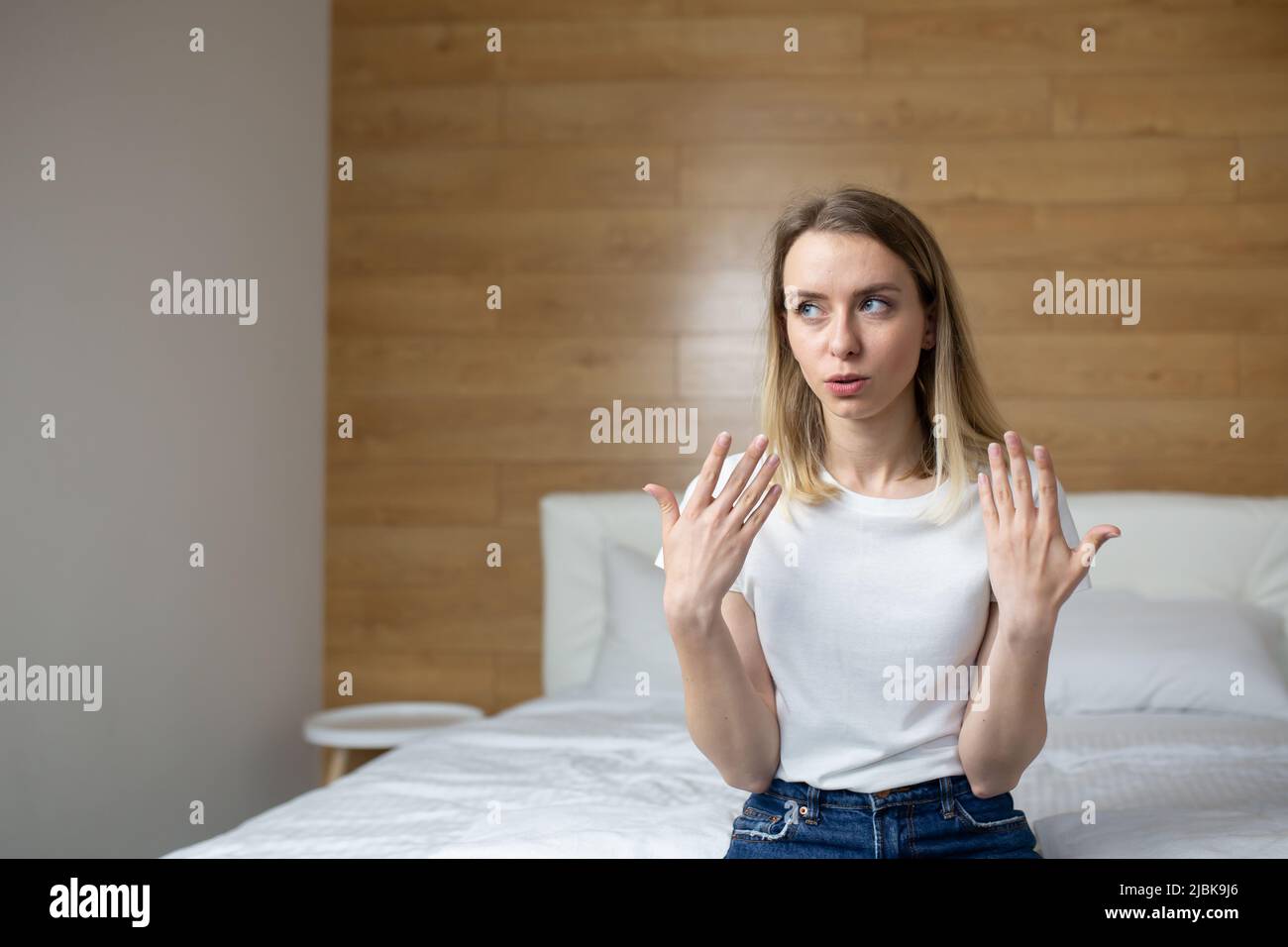 Giovane donna seduta sul letto di casa, in albergo, molto calda, agitando le braccia, respiro corto, respiro corto, malessere Foto Stock