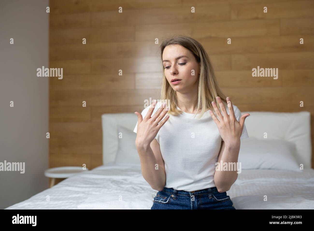 Giovane donna seduta sul letto di casa, in albergo, molto calda, agitando le braccia, respiro corto, respiro corto, malessere Foto Stock