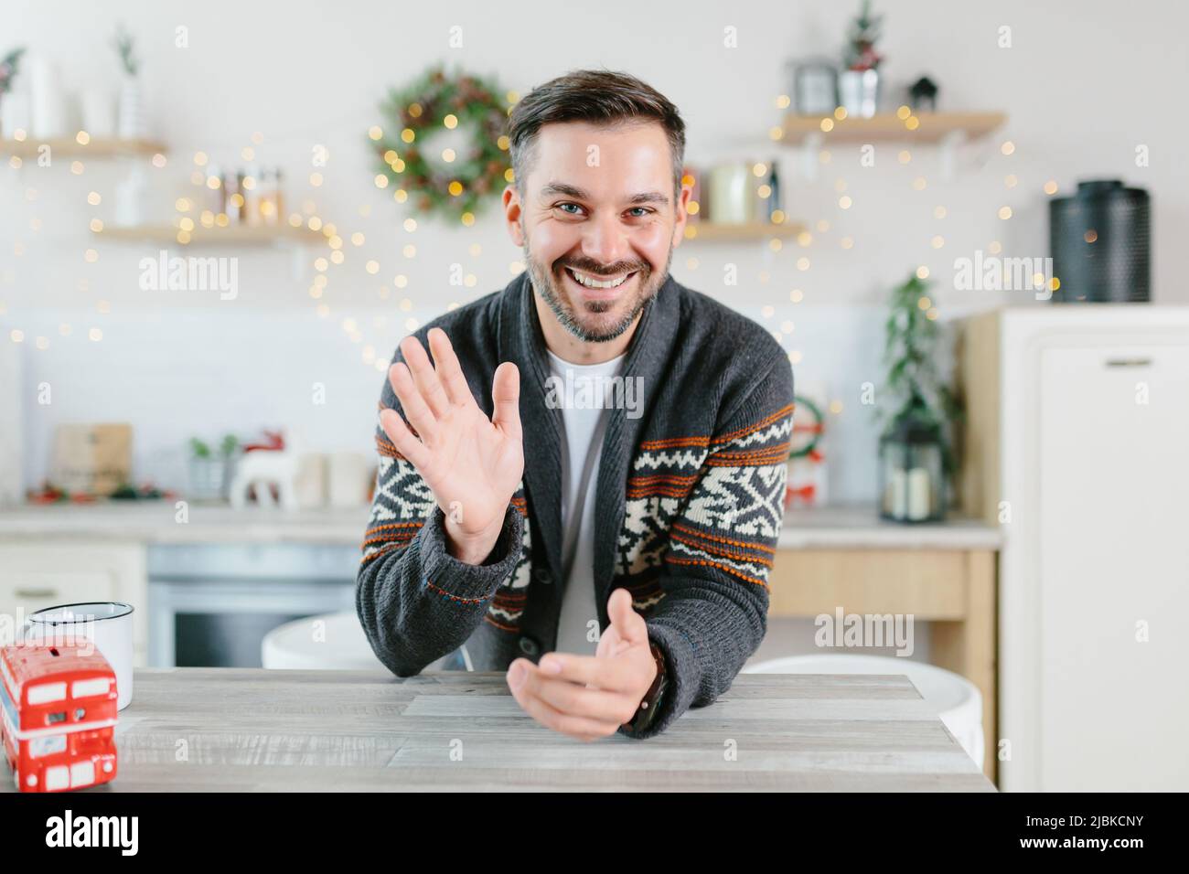 L'uomo a casa guarda la fotocamera e comunica tramite link video, guarda dalla webcam, saluta amici e colleghi con Natale e NE Foto Stock