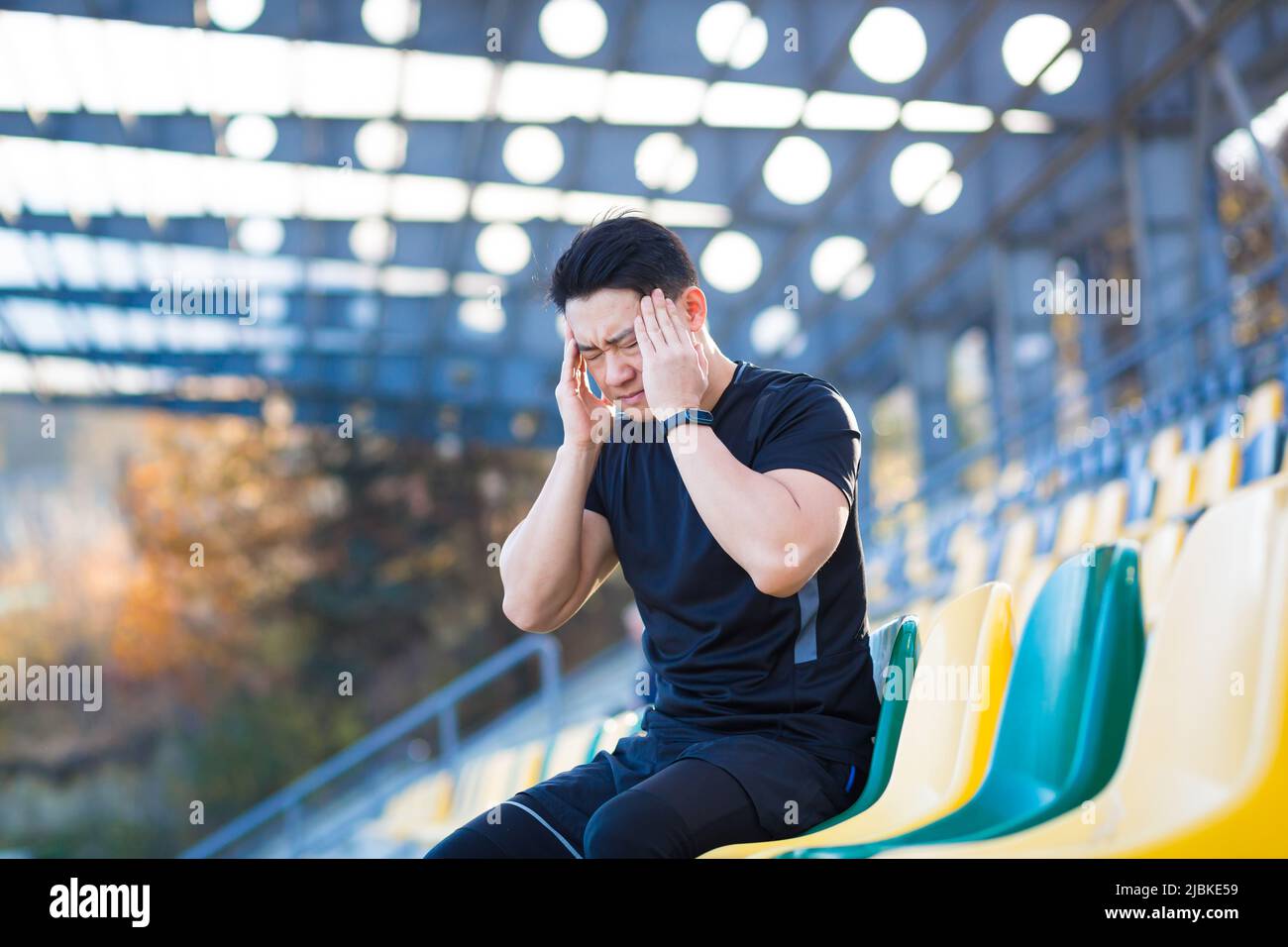 L'atleta maschio stanco che riposa, asiatico che tiene la testa, ha un mal di testa grave dopo la corsa Foto Stock