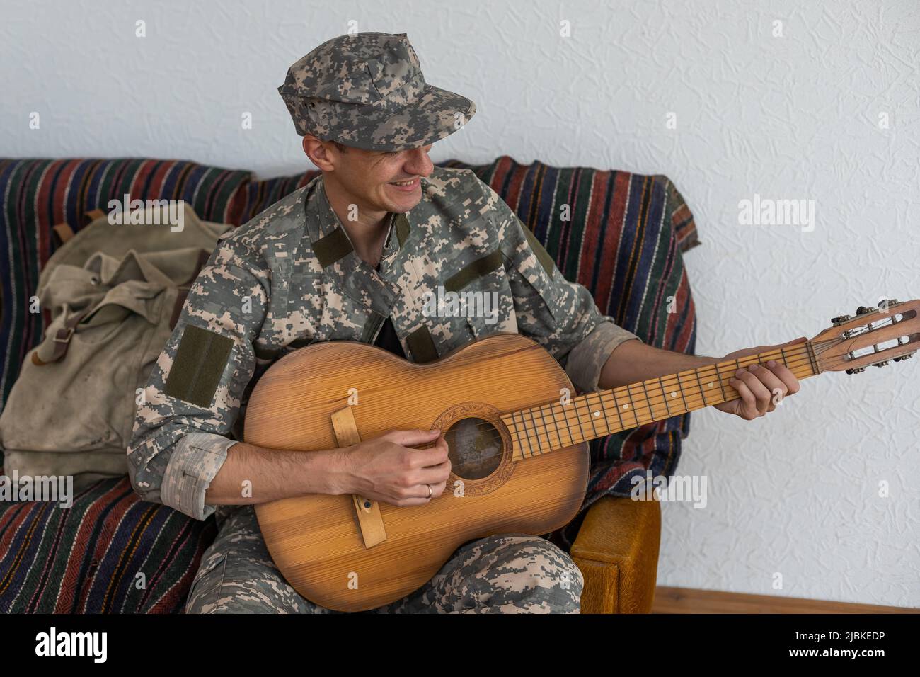 Veterano nel concetto di gioco della chitarra su sedia a rotelle. Riunione di famiglia. Figlio e moglie. Uniforme mimetica. Background familiare. Riposare insieme. Sensazioni che mostrano Foto Stock