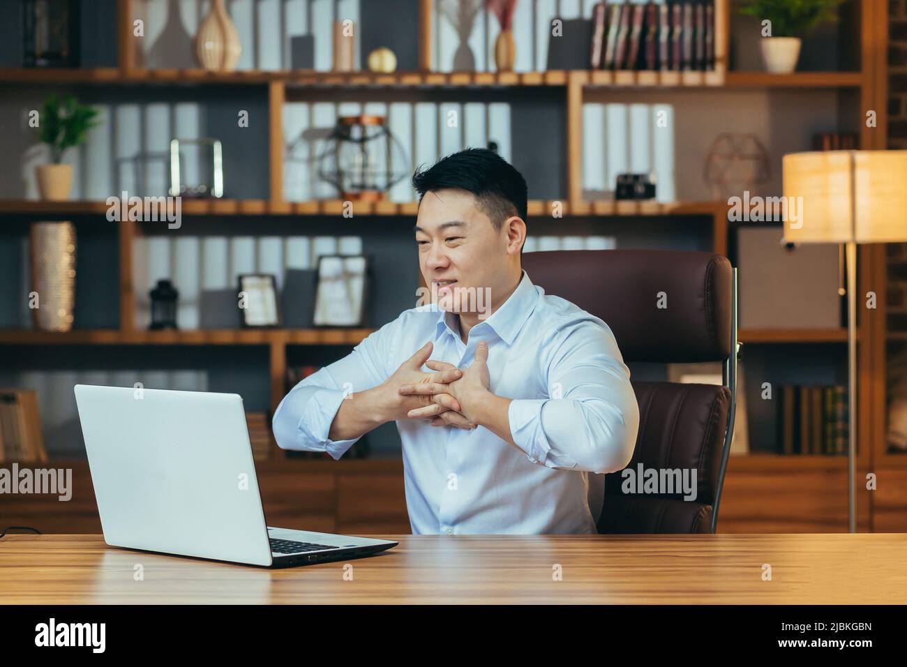 successo e felice boss asiatico guarda lo schermo del laptop e sorride, videochiamata con i colleghi, racconta piani finanziari, business meeting online Foto Stock
