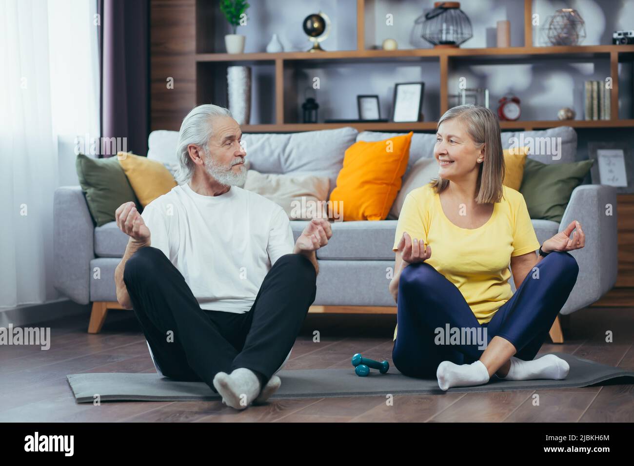 Coppia anziana uomo e donna insieme a casa praticando yoga meditating seduta sul pavimento in posizione lotus Foto Stock