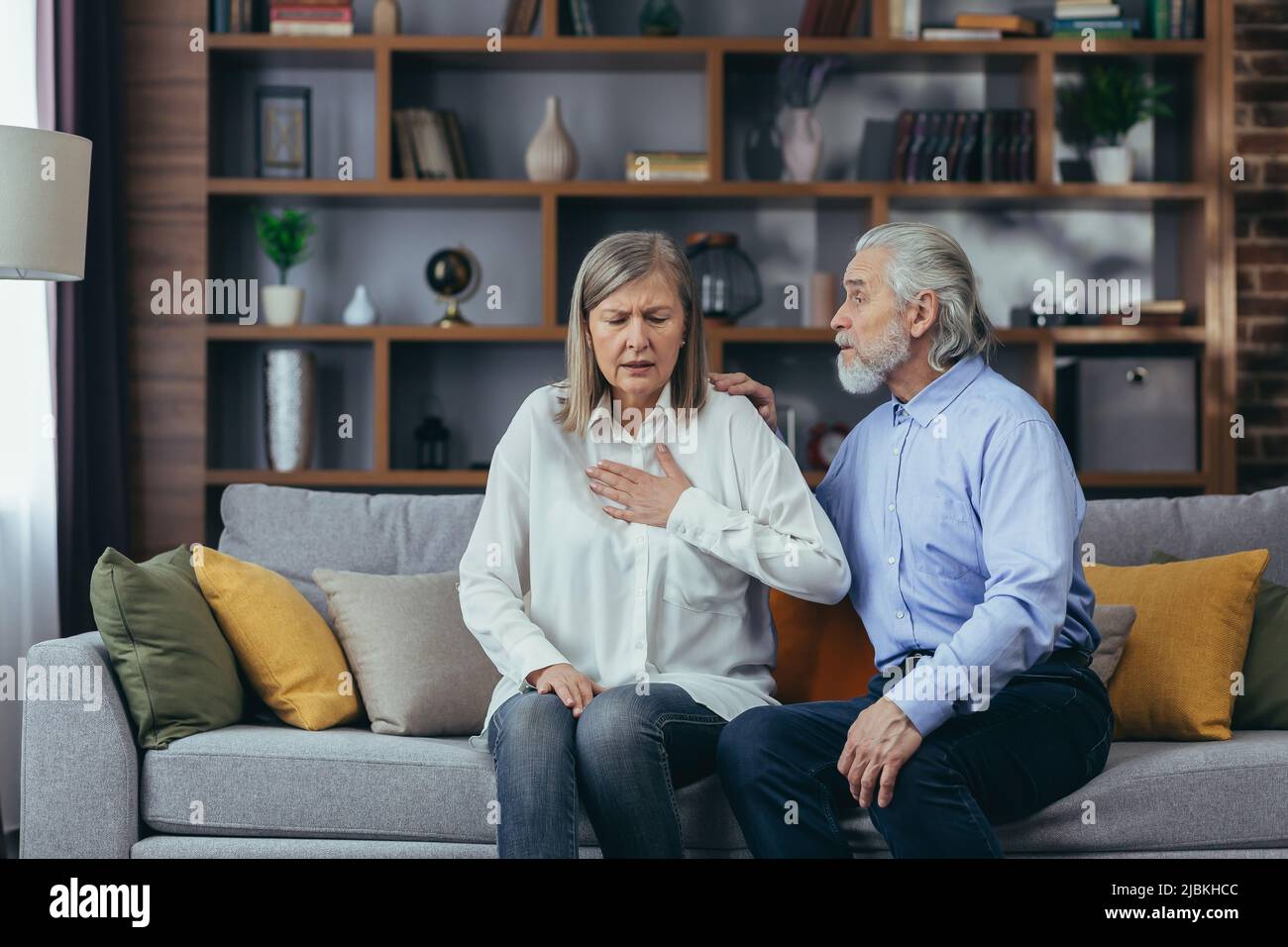 Coppia anziana a casa, la donna ha grave dolore toracico e respiro corto, marito cerca di calmare la moglie Foto Stock