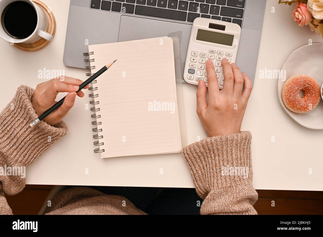 Vista dall'alto di una donna utilizzando una calcolatrice per calcolare il suo reddito mensile e le spese al suo tavolo di lavoro. Foto Stock