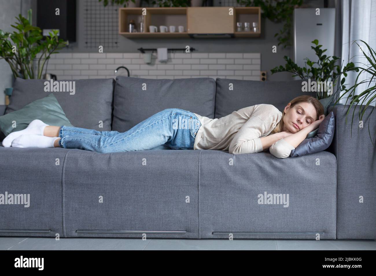 Donna bionda stanca di mezza età che dorme sul divano dopo il lavoro Foto Stock