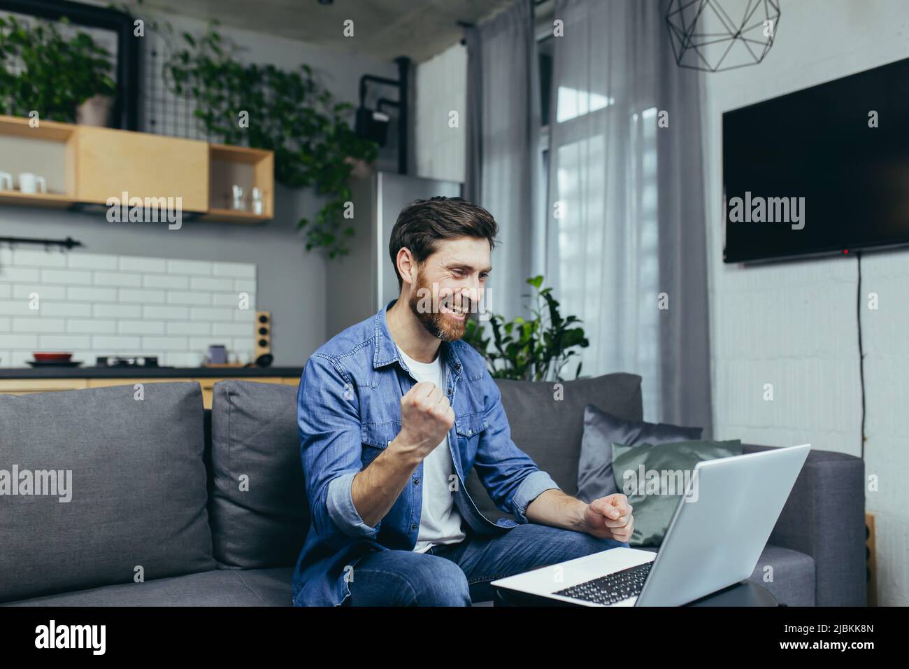 Felice uomo finito il lavoro sul progetto, felice di lavorare al computer, tenendo mano al gesto di vittoria, uomo a casa che lavora con il portatile Foto Stock