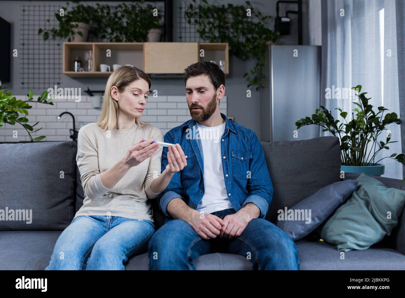 Uomo e donna tristi seduti sul divano, delusi da un test di gravidanza negativo Foto Stock