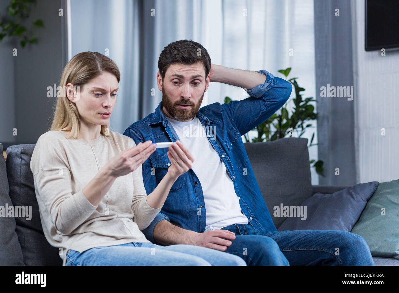 Uomo e donna tristi seduti sul divano, delusi da un test di gravidanza negativo Foto Stock