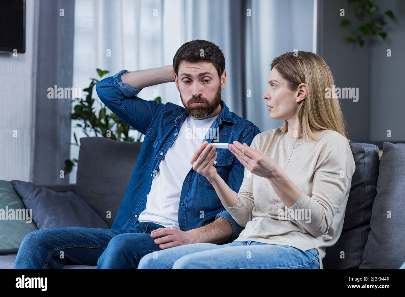 Uomo e donna tristi seduti sul divano, delusi da un test di gravidanza negativo Foto Stock