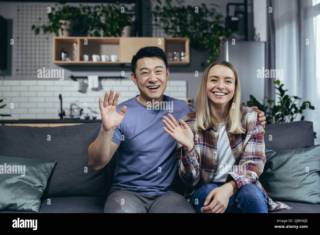 Coppia felice guardando la webcam e sorridendo chattando con gli amici online, uomo e donna di razze diverse, agitando mani gesto di congratulazioni, si Foto Stock