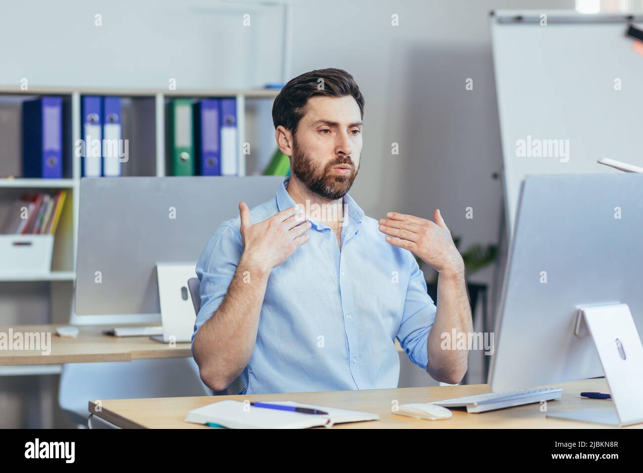 Caldo in ufficio, un uomo d'affari in una camicia che lavora in un luminoso ufficio moderno, agitando le braccia cercando di rinfrescarsi Foto Stock