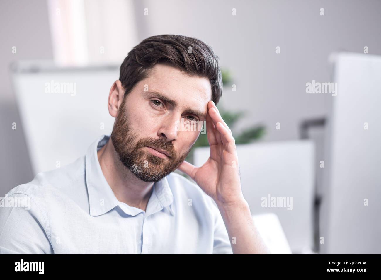 Verticale. Foto da vicino. Lavoratore da ufficio stanco e attento. Seduto su una scrivania in ufficio, al computer, tenendo la testa nelle mani, stanco, Foto Stock