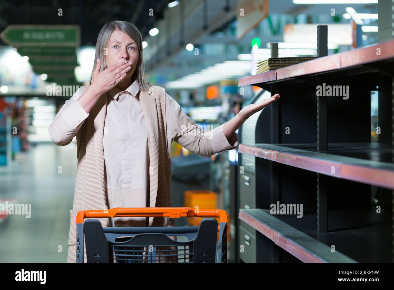 Quarantena, guerra, deficit. Donna anziana preoccupata e spaventata in un negozio, supermercato, si diffonde le braccia, punti a scaffali vuoti. Non ci sono prodotti in Foto Stock