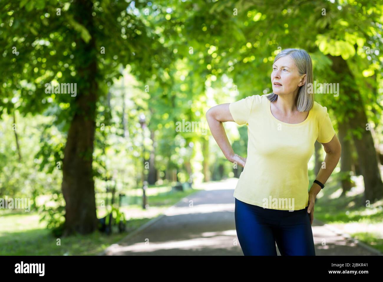 Donna attiva anziana in una passeggiata nel parco ha ferito la schiena, pensionato in uno scatto in una giornata estiva Foto Stock