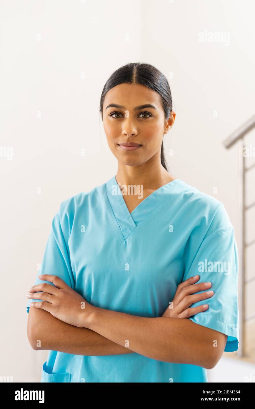 Ritratto di fidato medico biracale giovane femmina con le braccia incrociate in clinica Foto Stock