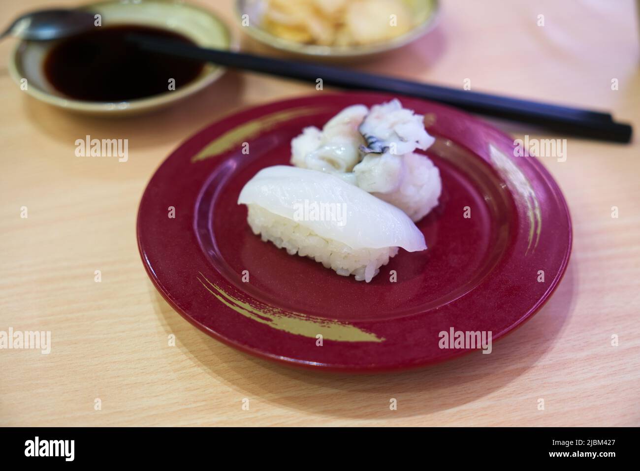 IKA nigiri sushi o sushi calamari freschi, calamari di sushi su piatto rosso con immagini sfocate di bacchette, salsa di soia o shoyu e zenzero. Foto Stock