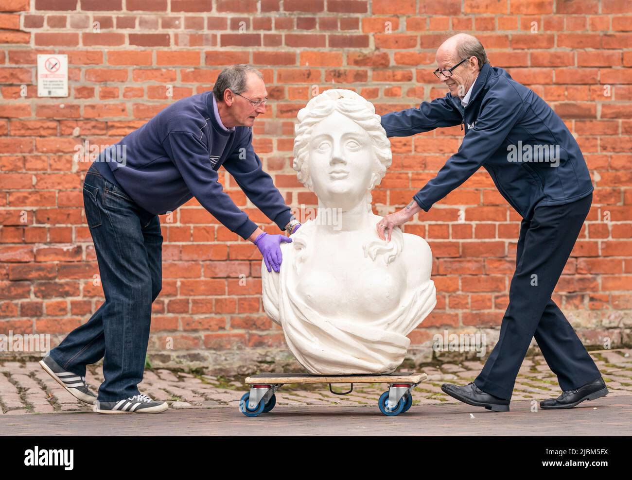 John Sutton (a sinistra) e Pete Forytarz (a destra) manovrano una testa di figura, mentre un gruppo di volontari svolge il lavoro di conservazione sulle teste di figura della nave e altri manufatti marittimi davanti a loro in mostra presso il rinnovato Hull Maritime Museum. Data foto: Martedì 7 giugno 2022. Foto Stock