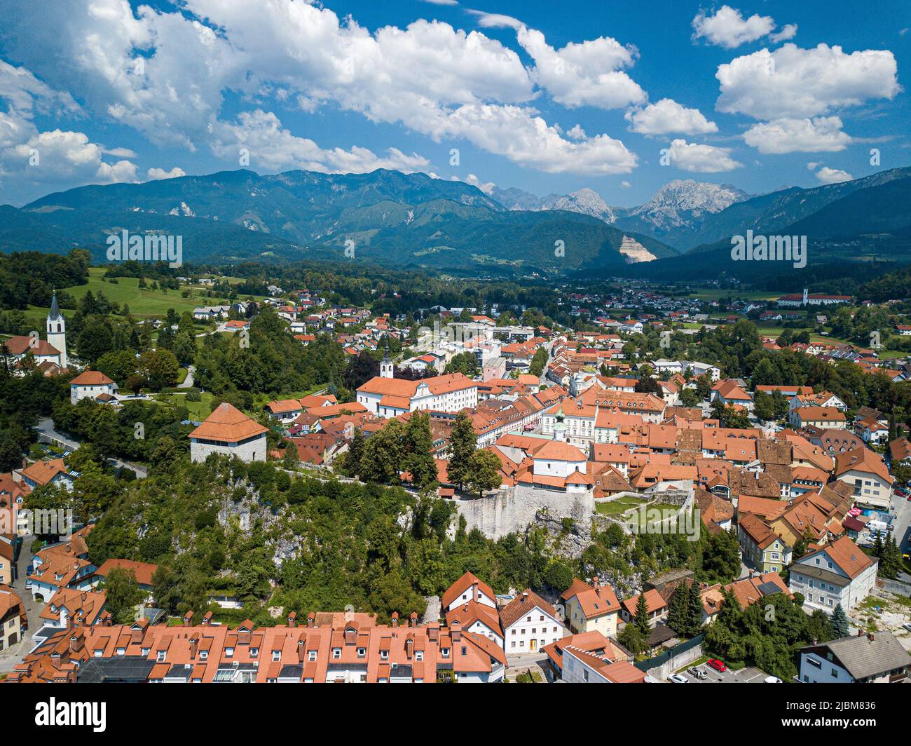 Vista sui droni della città di Kamnik con la chiesa di San Cantiano circondata da edifici con tetto rosso ai piedi delle lussureggianti montagne delle alpi Foto Stock