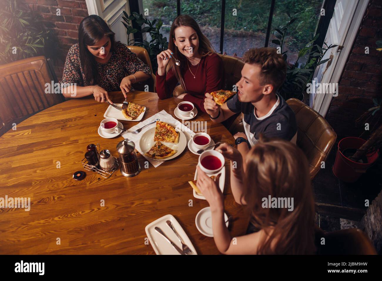 Scatto ad alto angolo di gruppo di migliori amici che hanno cenato a tavola rotonda insieme parlando e sorridendo in un caffè accogliente. Foto Stock