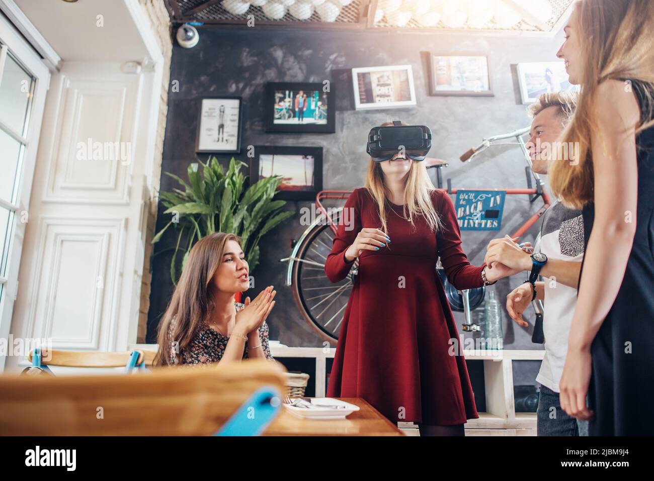 Gruppo di studenti che distribuiscono insieme ragazza guardando film in 3D occhiali di realtà virtuale, amici in attesa del loro turno in caffetteria. Foto Stock