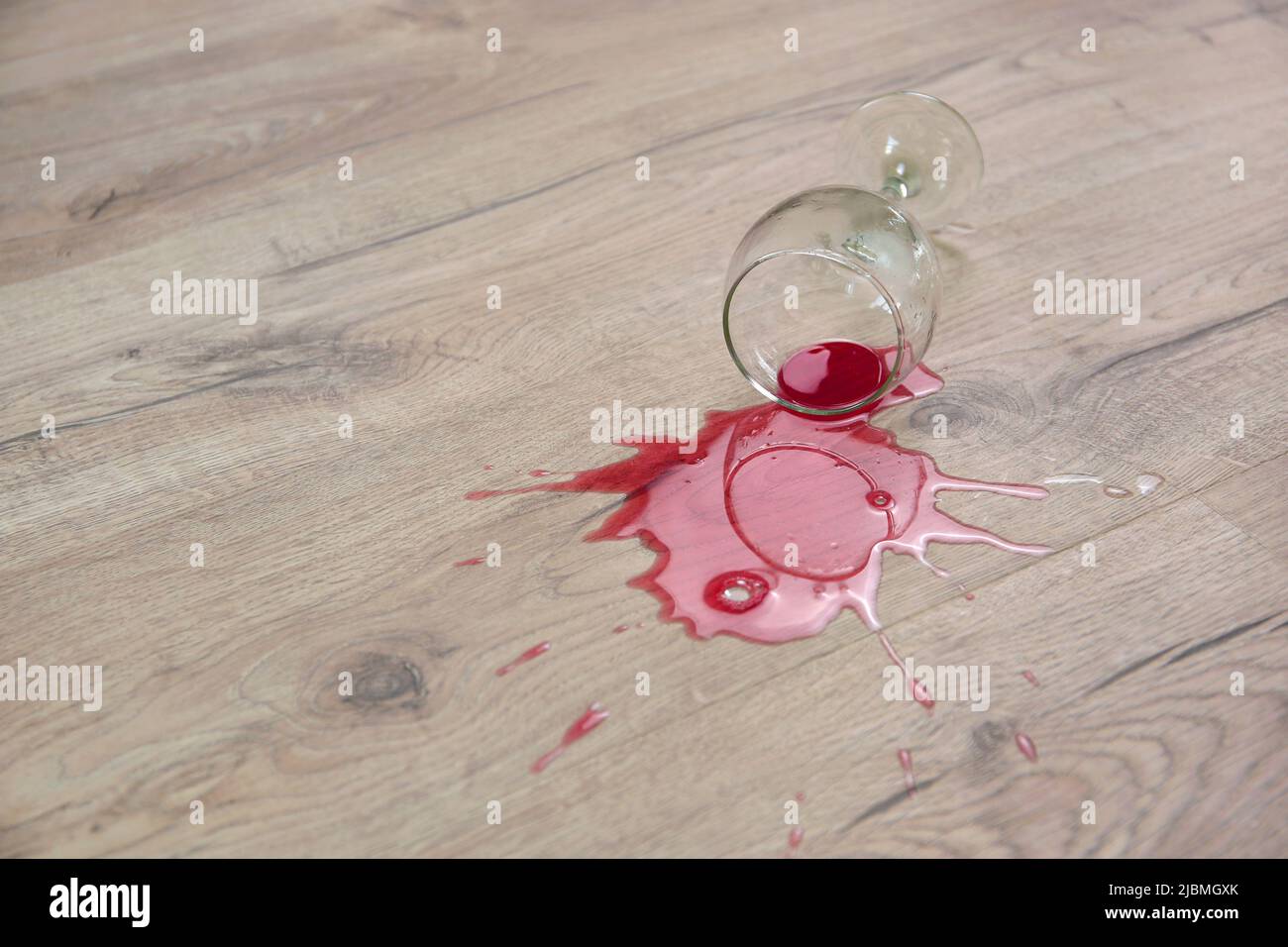 Un bicchiere di vino rosso cadde sul laminato, il vino versato sul pavimento. Foto Stock