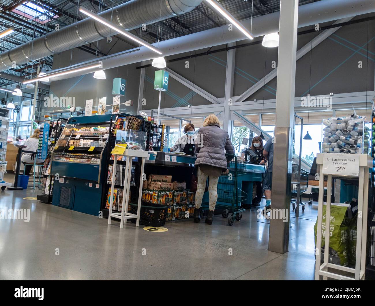 Kirkland, WA USA - circa Settembre 2021: Vista angolata di una donna che guarda fuori con un cassiere che indossa una maschera facciale all'interno di un intero mercato Foods. Foto Stock Kirkland, WA USA - circa Settembre 2021: Vista angolata di una donna che guarda fuori con un cassiere che indossa una maschera facciale all'interno di un intero mercato Foods. Foto Stock