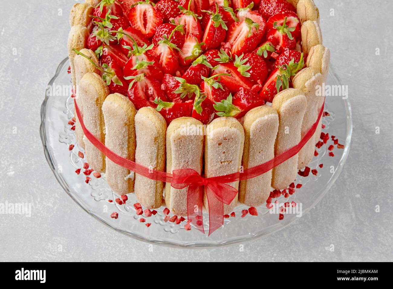Torta con fragole, biscotti savoiardi e mascarpone legati con un nastro rosso su un tavolo di cemento chiaro Foto Stock