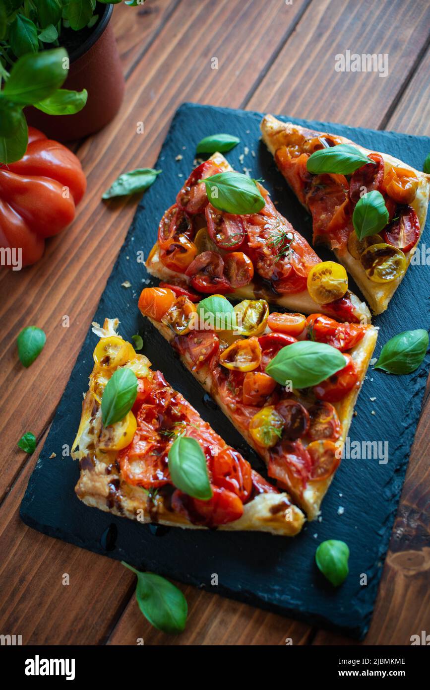 Torta di pasta sfoglia al pomodoro con aceto balsamico e basilico fresco su piastra di pietra Foto Stock