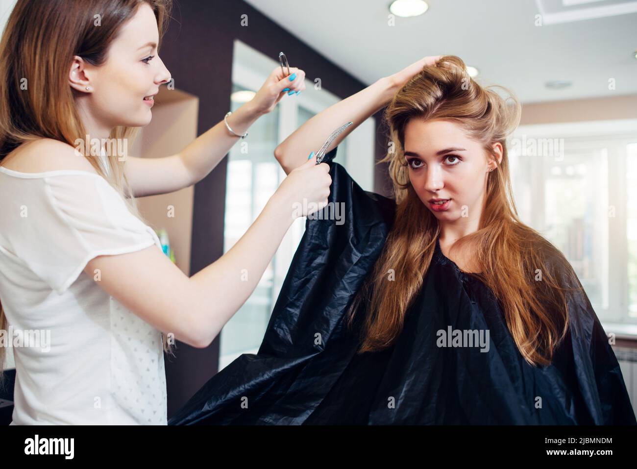 Sorridente femmina parrucchiere che fa coiffure a bella giovane donna con capelli lunghi e leali in parrucchiere. Foto Stock