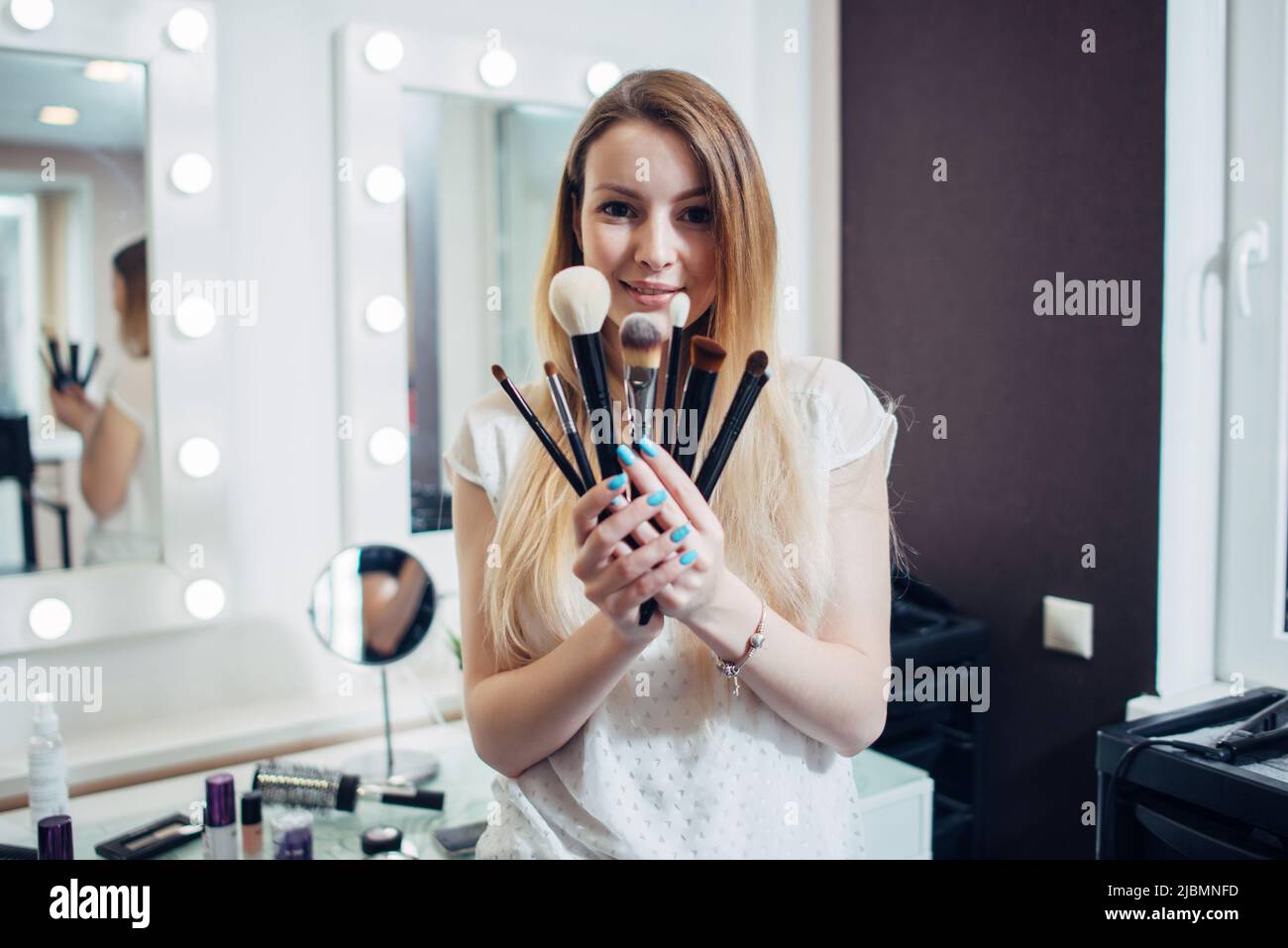 Ritratto di giovani artisti make-up che mostrano le sue spazzole guardando la macchina fotografica in studio di bellezza. Foto Stock