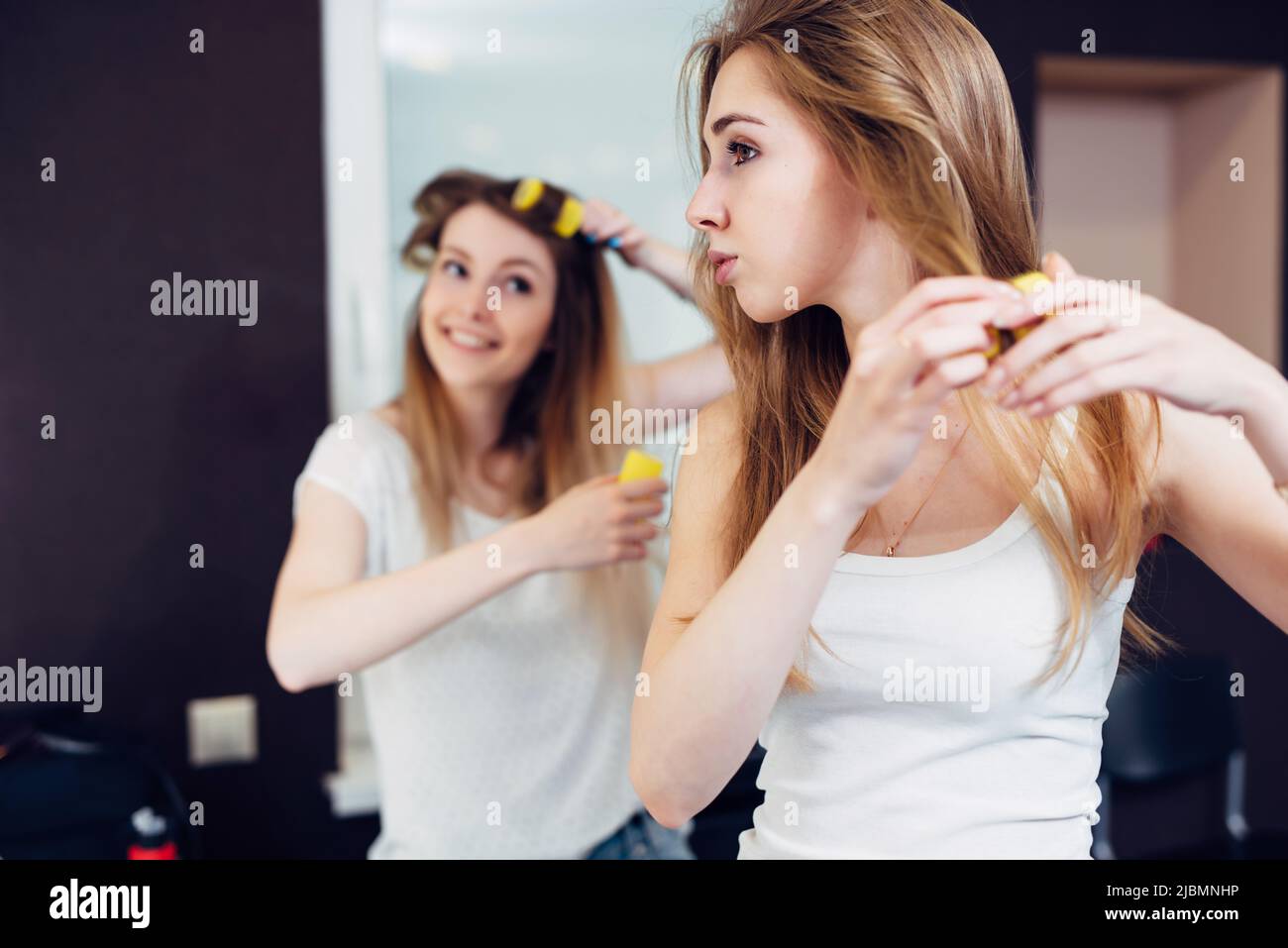 Due amiche allegre che mettono i capelli in curlers a casa. Foto Stock