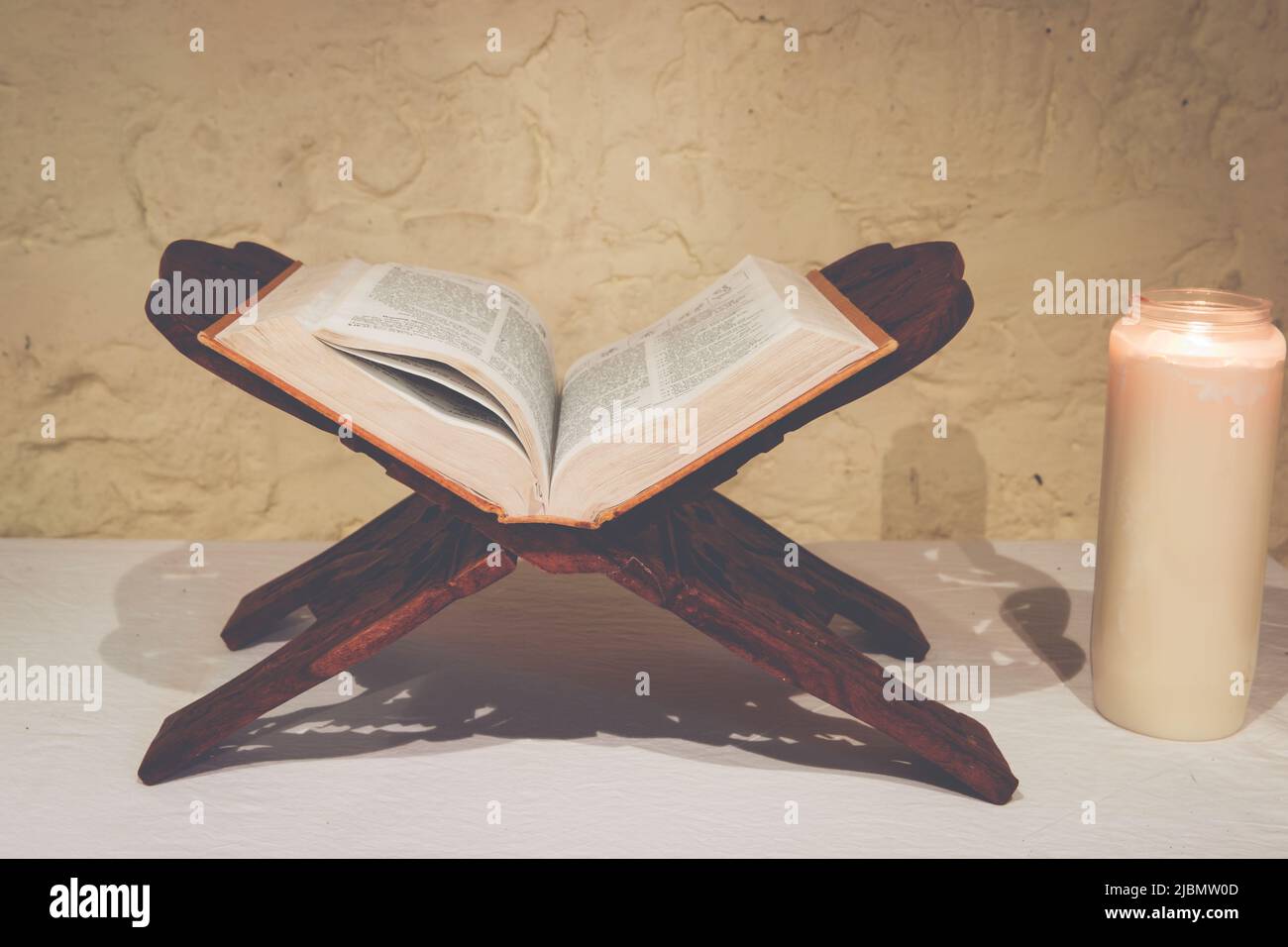 Aprire la Sacra Bibbia su ornato libro stand in legno con candela in ambiente ascetico per la meditazione e la contemplazione Foto Stock