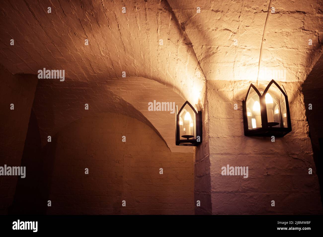 Seminterrato della chiesa gotica scuro con soffitto a volta a groin. Colonna di mattoni e lanterne di candele di Faux Foto Stock