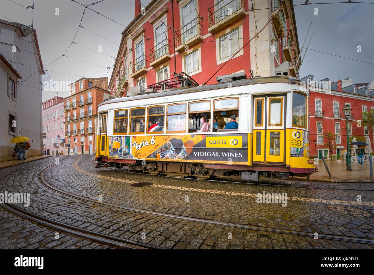 Un tradizionale tram giallo perora una curva su una strada bagnata di ciottoli nel centro di Lisbona, la capitale del Portogallo Foto Stock