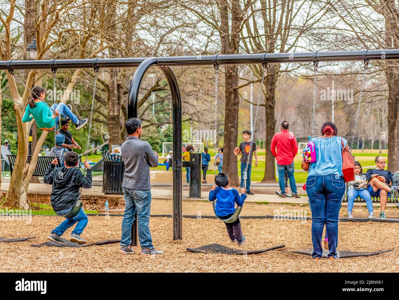 Charlotte, NC/USA - 24 marzo 2019: Famiglie che si divertono insieme nel Freedom Park. I bambini che oscillano sulle altalene mentre i loro genitori guardano in modo protetto. Foto Stock