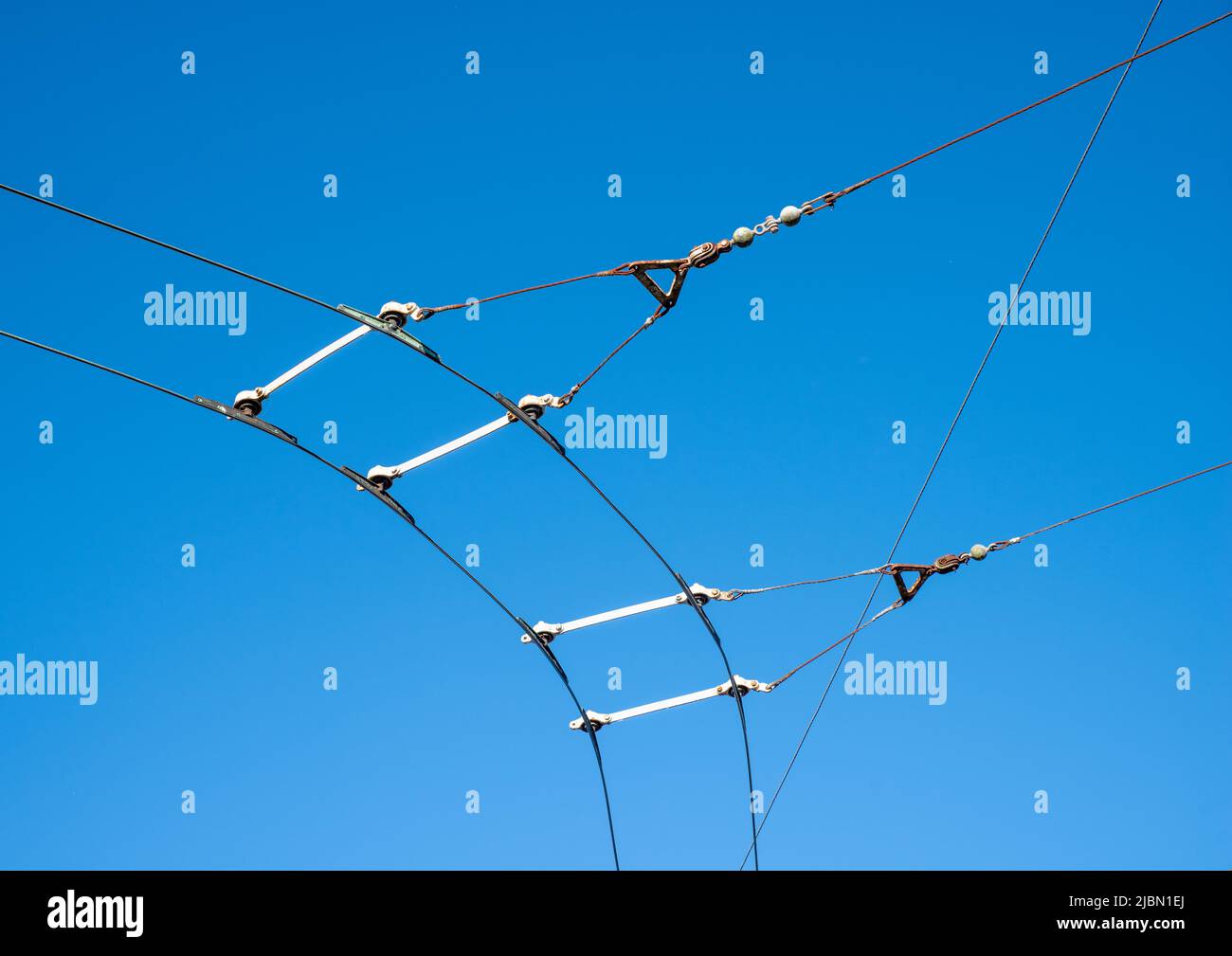 Cavi di catenaria e di contatto sospesi per un sistema di bus trolley elettrico su una curva con fondo cielo blu. Foto Stock