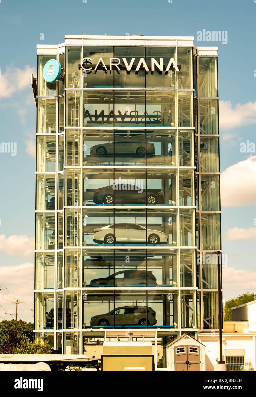 Il distributore automatico di auto a torre di vetro di Carvana è pieno di veicoli in attesa di essere prelevati dagli acquirenti con marchio in cima e cielo parzialmente nuvoloso. Foto Stock
