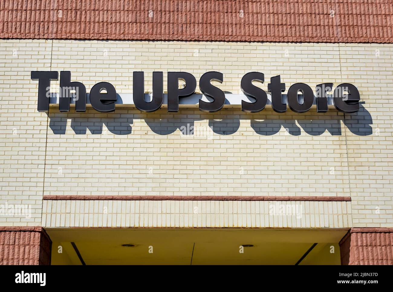 Marchio e logo della facciata esterna dell'UPS Store con lettere nere su mattoni beige con finiture color marrone chiaro e ombre. Foto Stock